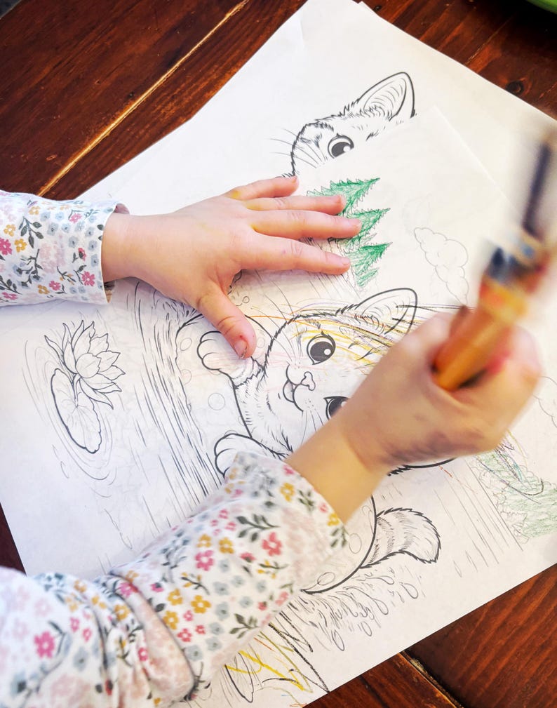 May include: A child's hands coloring a detailed cat illustration with a paintbrush. The coloring book page features a cat in a pond with a lily pad. The child's sleeve has a floral pattern.
