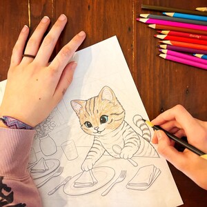 May include: A person coloring a detailed drawing of a cartoon cat with a pencil. The cat is tan and brown with blue eyes, sitting at a table setting. A collection of colored pencils is in the background.