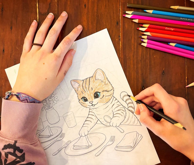 May include: A person coloring a detailed drawing of a cartoon cat with a pencil. The cat is tan and brown with blue eyes, sitting at a table setting. A collection of colored pencils is in the background.