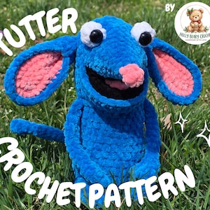 May include: A blue crochet creature with large ears, a pink nose, and black eyes. The text "TUTTER CROCHET PATTERN" is displayed in white. The image is set against a backdrop of green grass.
