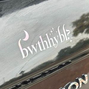 May include: A white ceramic mug with a black handle and the text "But First, Coffee" in a black, bold font. The mug is sitting on a wooden surface.