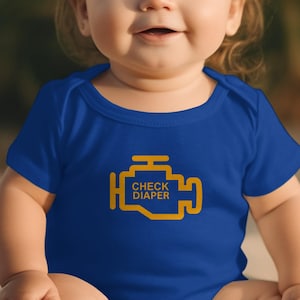 May include: A blue baby bodysuit featuring a yellow engine graphic with the text "CHECK DIAPER". The short-sleeved bodysuit has a round neck. The baby is smiling.