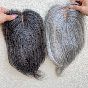 May include: Two gray hair toppers are displayed side-by-side. One is a dark gray, almost black, and the other is a lighter silver-gray. Both have a natural-looking part and are held up by hands, showcasing the hair's texture and color variations.
