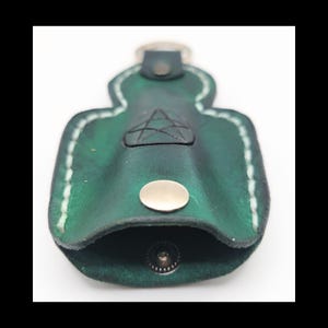 May include: Green leather keychain holder with white stitching and a silver snap closure. The holder features a pentagram design and a metal key ring. The leather has a distressed look.