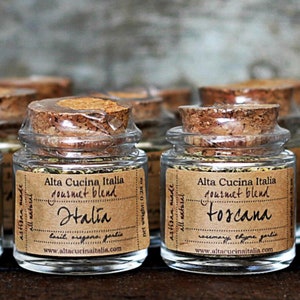 May include: Four small glass jars with cork lids filled with dried herbs. The jars are labelled with brown paper labels that say "Alta Cucina Italia gourmet blend" and the names of the blends: "Halia" and "Toscana".