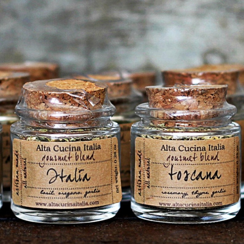 May include: Four small glass jars with cork lids filled with dried herbs. The jars are labelled with brown paper labels that say "Alta Cucina Italia gourmet blend" and the names of the blends: "Halia" and "Toscana".