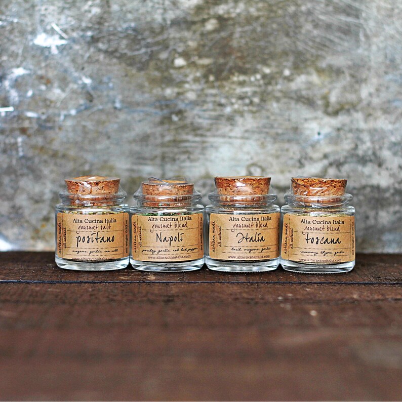 May include: Four small glass jars with cork tops, each containing a different blend of herbs and spices. The jars are labelled with the names "Positano", "Napoli", "Halia", and "Toscana".