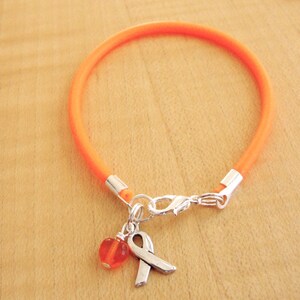 May include: Orange cord bracelet with a silver charm featuring a small orange bead and a silver ribbon.
