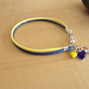 May include: A yellow and blue braided bracelet with a silver charm that says "HOPE" and two heart-shaped beads, one yellow and one blue.