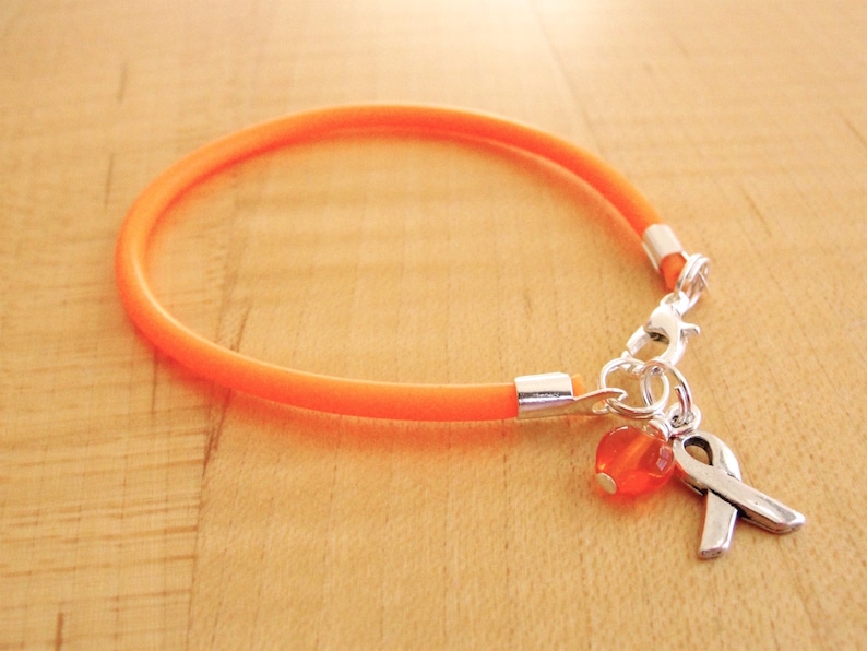 May include: Orange silicone bracelet with a silver charm featuring an orange bead and a silver ribbon.