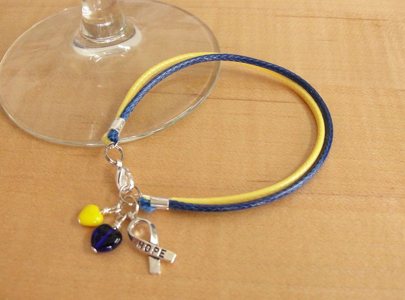 May include: A yellow and blue cord bracelet with a silver charm that says "HOPE" and two heart-shaped beads, one yellow and one blue.