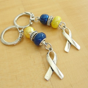 May include: Two silver keychains with blue and yellow beads and silver ribbon charms. The ribbons are tied in a bow.