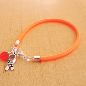 May include: Orange silicone bracelet with a silver charm featuring a red heart and a ribbon with the word "HOPE" engraved on it.