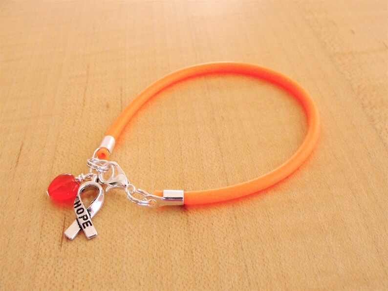 May include: Orange silicone bracelet with a silver charm featuring a red heart and a ribbon with the word "HOPE" engraved on it.