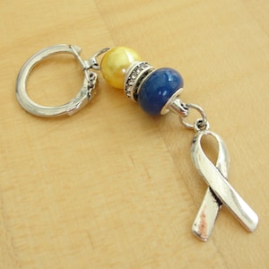 May include: A silver key chain with a blue and yellow bead charm and a silver ribbon charm.
