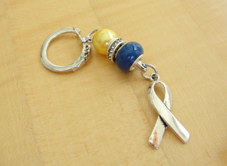 May include: A silver key chain with a blue and yellow bead charm and a silver ribbon charm.