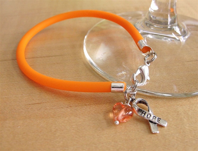 May include: Orange silicone bracelet with a silver clasp and a charm featuring a small orange heart and a silver ribbon with the word "HOPE" engraved on it.