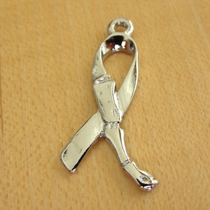 May include: Silver-toned metal charm shaped like a ribbon. The ribbon is tied in a bow and has a loop at the top for attaching to a necklace or bracelet.