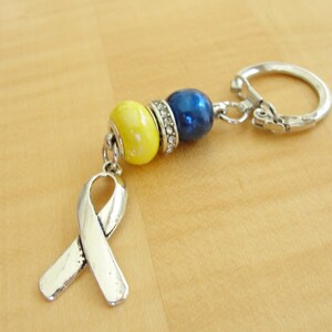 May include: A silver key chain with a yellow and blue bead charm and a silver ribbon charm.