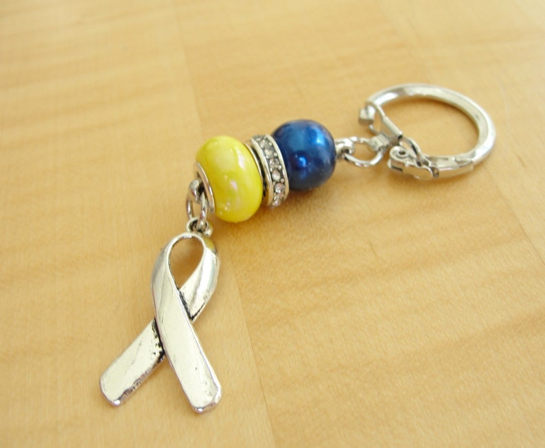 May include: A silver key chain with a yellow and blue bead charm and a silver ribbon charm.