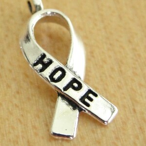 May include: Silver charm in the shape of a ribbon with the word "HOPE" engraved on it.