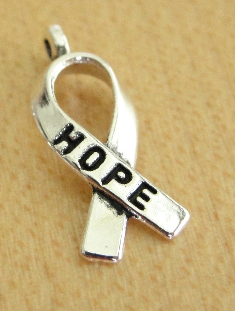 May include: Silver charm in the shape of a ribbon with the word "HOPE" engraved on it.
