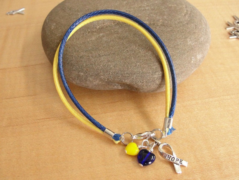 May include: A yellow and blue friendship bracelet with a silver charm that says "HOPE" and two heart charms, one yellow and one blue.