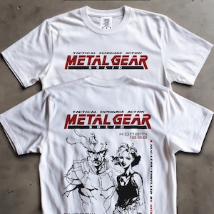 May include: White t-shirts featuring the text "METAL GEAR SOLID" in red and black. One shirt displays the text on the front. The other shirt has a graphic of characters and text on the back, including "KONAMI 1998" and "A NUCLEAR THRILLER BY HIDEO KOJIMA."