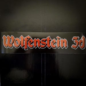 May include: A rectangular sticker with the text "Wolfenstein 3d" in a stylized, orange and red font with a white outline. The sticker is on a black background.