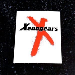 May include: Square white sticker with the word "Xenogears" in black font, overlaid on a large, red, brushstroke-style "X" shape. The sticker is on a dark, speckled surface.