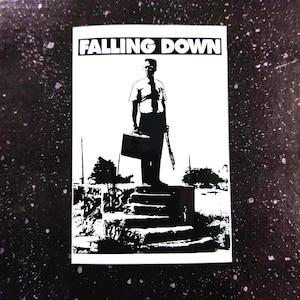 Può includere: Grafica in bianco e nero con la scritta "FALLING DOWN" sopra un'illustrazione di un uomo che tiene una valigetta e un'arma. L'uomo è in piedi su dei gradini, su sfondo scuro.