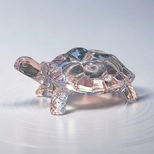 Puede incluir: Una figura de tortuga de cristal transparente con un caparazón y patas detalladas. La figura es transparente, permitiendo el paso de la luz, y se encuentra sobre una superficie blanca. El diseño de la tortuga es intrincado, mostrando su forma.