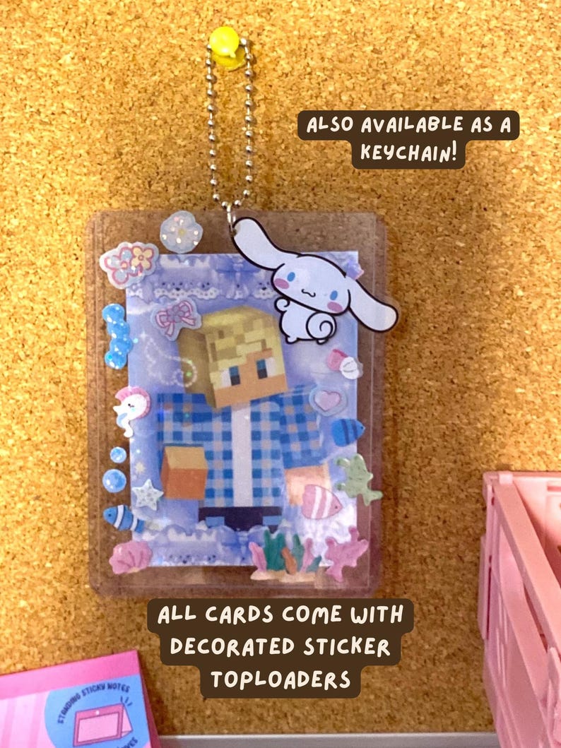May include: A clear plastic toploader holding a card with a blocky, pixelated character wearing a blue plaid shirt. The toploader is decorated with various small stickers including a white cartoon dog, shells, and fish. Text reads: ALSO AVAILABLE AS A KEYCHAIN! and ALL CARDS COME WITH DECORATED STICKER TOPLOADERS.