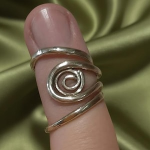 Könnte beinhalten: Ein silberfarbener Ring mit einem Spiraldesign. Der Ring umschließt den Finger und weist eine zentrale Spirale und eine glatte, polierte Oberfläche auf. Der Ring ist ein Schmuckstück.