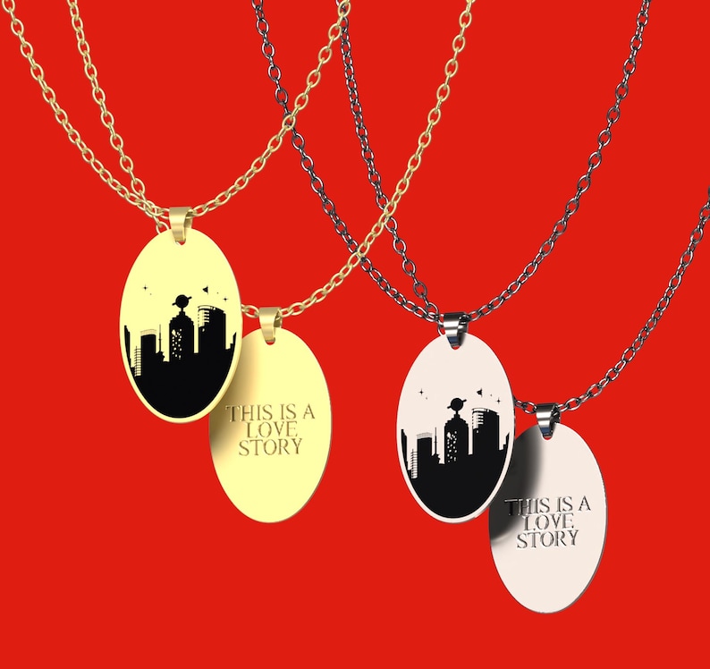 Peut inclure: Quatre colliers avec des pendentifs ovales. Deux sont dor&eacute;s, deux sont argent&eacute;s. Chaque pendentif pr&eacute;sente une silhouette de paysage urbain noir et le texte "THIS IS A LOVE STORY". Le fond est rouge uni.