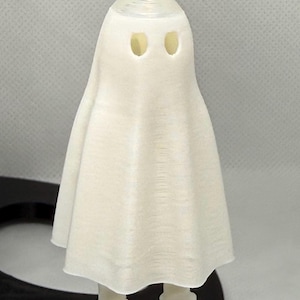 Peut inclure: Un porte-clés blanc en forme de fantôme. Le fantôme a deux trous pour les yeux et un corps drapé en forme de drap. Le porte-clés est fabriqué dans un matériau imprimé en 3D et possède une boucle en métal argenté.