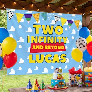 May include: A light blue party backdrop featuring a white cloud pattern, a colorful pennant banner, and the text TWO INFINITY AND BEYOND LUCAS. The scene includes a Toy Story themed cake, gift boxes, and a cluster of blue, yellow, red, and cow-print balloons.
