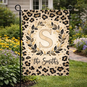 May include: A decorative garden flag with a leopard print background. The flag features a large letter "S" in a wreath, with the words "the Smiths" below. The flag is displayed on a black metal stand.