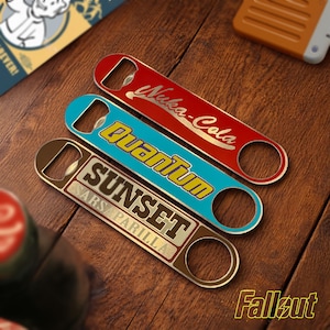 Peut inclure: Trois ouvre-bouteilles en métal avec des motifs sur le thème de Fallout. Les ouvre-bouteilles sont rouges, bleus et marron, chacun avec un logo et un texte différents : "Nuka-Cola", "Quantum" et "Sunset Sarsaparilla". Le logo Fallout est en bas à droite.