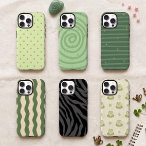 May include: Six smartphone cases arranged in two rows. Top row: light green with small stars, light green with a spiral pattern, and dark green with horizontal stripes and dots. Bottom row: green wavy stripes, black and gray zebra print, and a grid pattern with small frogs.