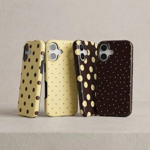 May include: Four phone cases with a polka dot pattern. Two cases are light yellow with brown dots, and two are dark brown with cream-colored dots. The cases are standing upright against a neutral background.