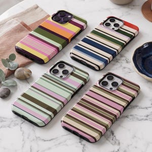 May include: Four rectangular smartphone cases featuring horizontal stripes in various color palettes including pink, olive green, orange, navy blue, and cream. Each case has a cutout for a triple-lens camera system and a charging port at the base.