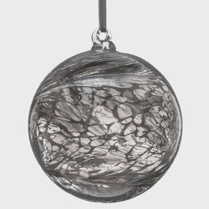 Puede incluir: Una bola de Navidad de cristal transparente con un patr&oacute;n arremolinado y texturizado en tonos grises y plateados. El adorno es redondo y tiene un lazo para colgar con una cinta gris.