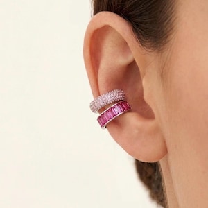 Puede incluir: Dos pendientes tipo ear cuff apilados en el cartílago. El superior presenta un engaste pavé de pequeñas piedras rosa claro. El inferior está elaborado en metal plateado y cuenta con una hilera de piedras rosa intenso de corte baguette.