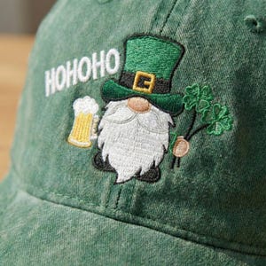 May include: Green baseball cap with an embroidered St. Patrick's Day gnome design. The gnome wears a green hat and holds a beer and shamrocks. The word "HOHOHO" is embroidered above the gnome.