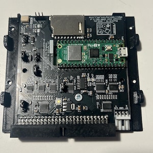 Könnte beinhalten: Eine schwarze Leiterplatte mit einem grünen Raspberry Pi Pico 2 W Mikrocontroller, einem silbernen SD-Kartenslot und verschiedenen elektronischen Bauteilen. Die Platine ist auf einem schwarzen 3D-gedruckten Rahmen montiert und trägt die Aufschrift BlueSCSI V2.