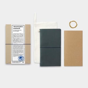 May include: A Traveler's Notebook set includes a dark teal leather cover, a kraft paper refill, a canvas pouch, and a rubber band. The packaging features text in English and Japanese. The notebook is designed for travelers.
