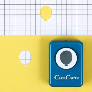Könnte beinhalten: Ein blauer CarlaCraft®-Papierstanzer in Ballonform mit einem gelben Ballonausschnitt und einem Ballonausschnitt aus Papier. Der Stempel hat einen weißen Kreis mit einer grauen Ballonform im Inneren. Der Hintergrund ist gelb und weißes kariertes Papier.