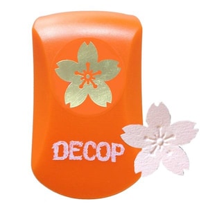May include: An orange paper punch featuring a gold cherry blossom design and the word "DECOP" in white. A cut-out paper cherry blossom is next to the punch. Suitable for scrapbooking and paper crafts.