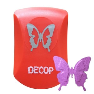 May include: A red craft punch with a butterfly design and the word "DECOP" in white. A purple butterfly is next to the punch. The butterfly design on the punch is a butterfly made of two faces.